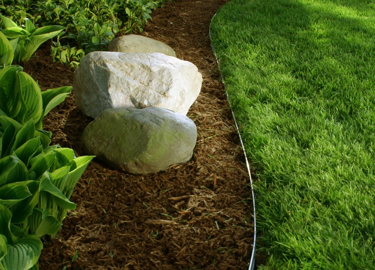 This image depicts a landscape bed with grass, mulch, rocks and plants using Permaloc landscape edging.