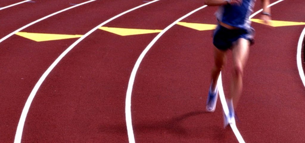 This image depicts a person running on a red, white and yellow sports track with Permaloc landscape edging.
