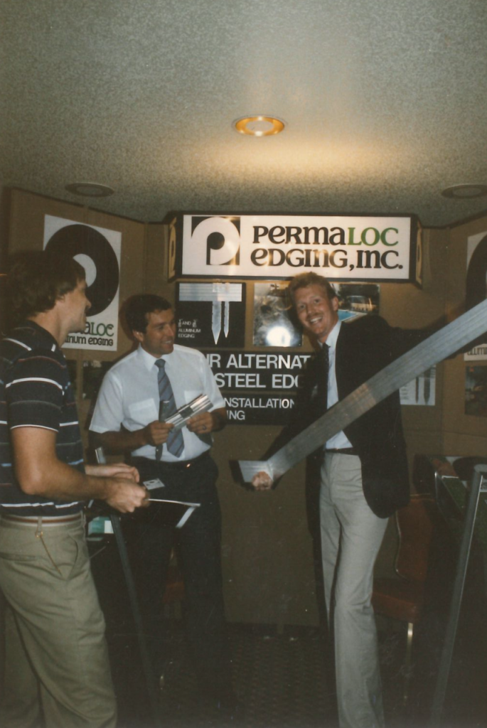 Dan Zwier, founder of Permaloc, holds his aluminum edging solution next to Permaloc signage.